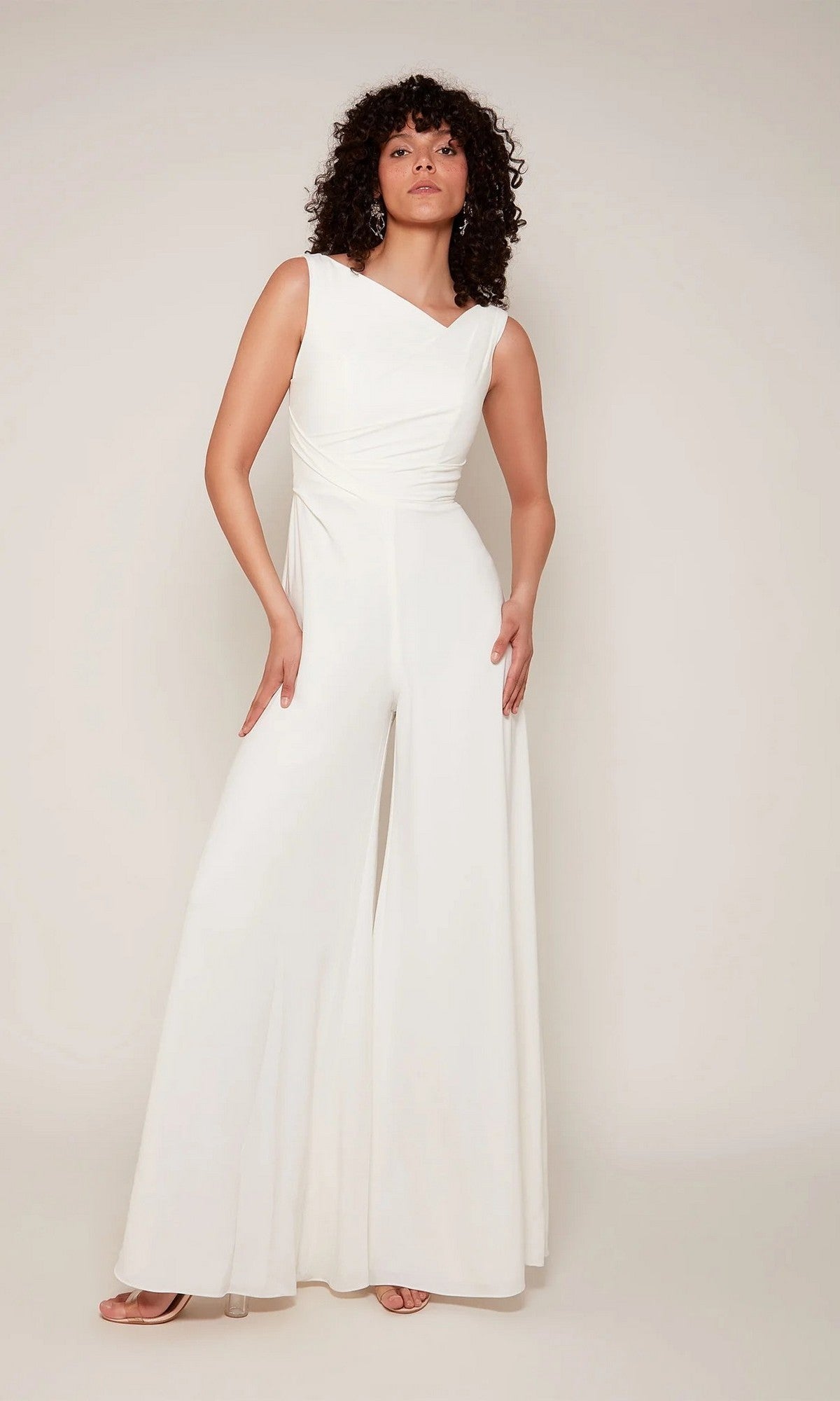 A person with curly hair wears the Alyce 70052 long white jumpsuit with open-toe heels, posing against a plain light background.